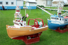 670: A model boat on Lawrence Barry's front lawn in St. Bride's. The boats are large, each  being several feet in length, and are entirely handmade by Mr. Barry. That's him sitting  in front of his workshop at upper left. (2004)